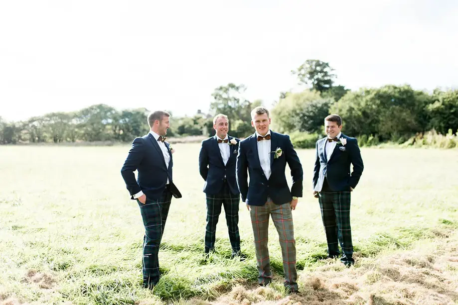 Groomsmen in matching tartan and feather bowtie groomswear stand on field