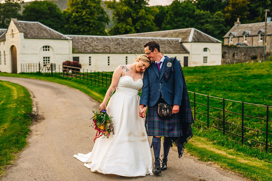 A couple holding hands and walking through a farm on their wedding day