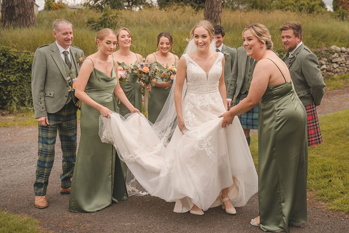 A group of people help a bride with the long skirt and train of her wedding dress