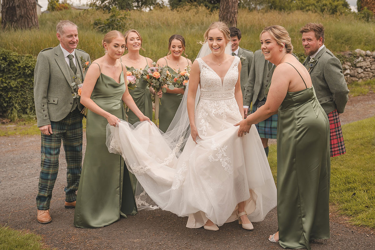 A group of people help a bride with the long skirt and train of her wedding dress