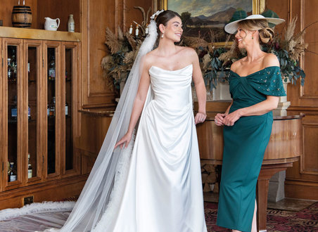 A bride wearing a strapless white wedding dress and long veil and a mother of the bride wearing forest green dress