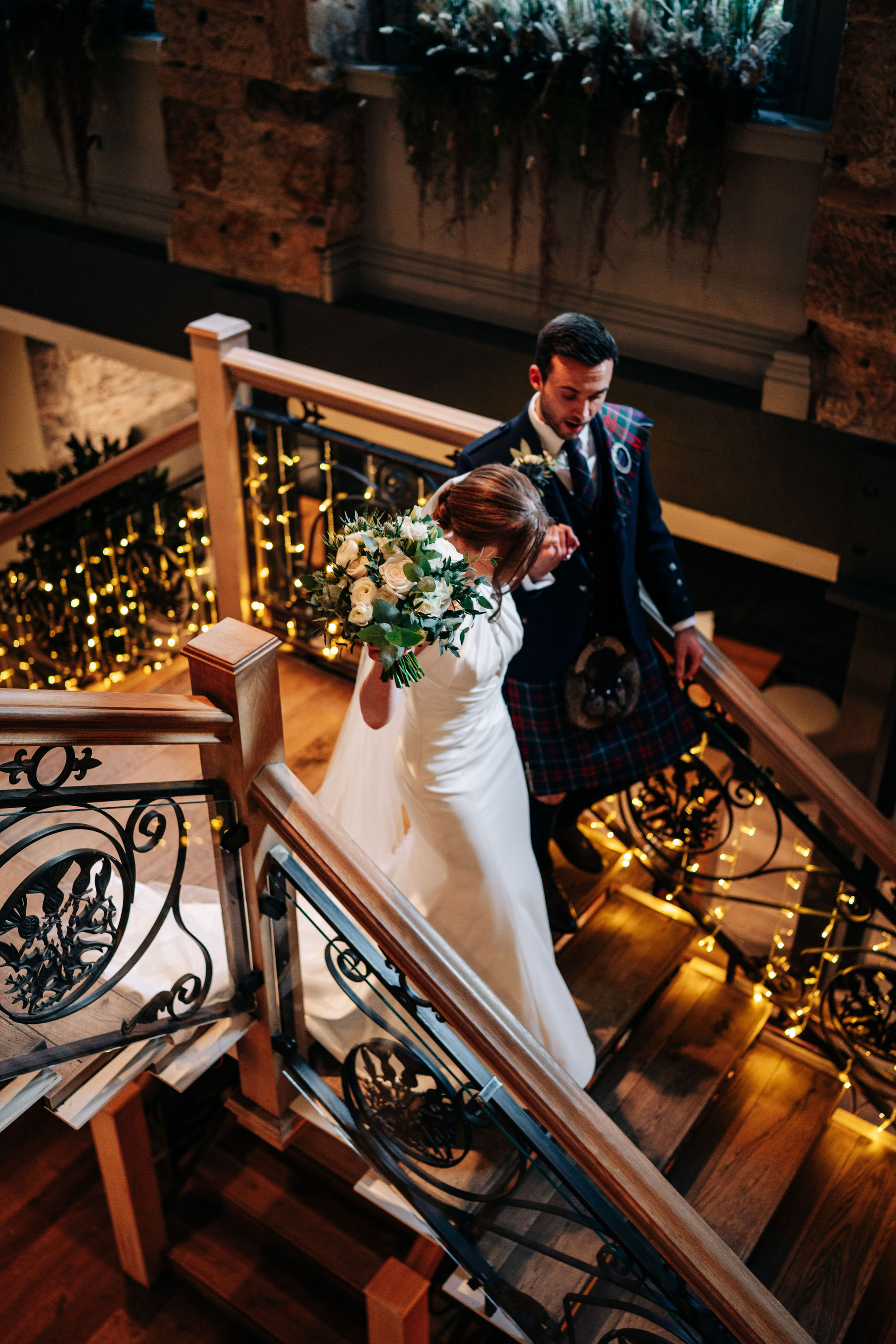 bride holding a bouquet of flowers holds hand with groom as they walk down staircase at citation glasgow