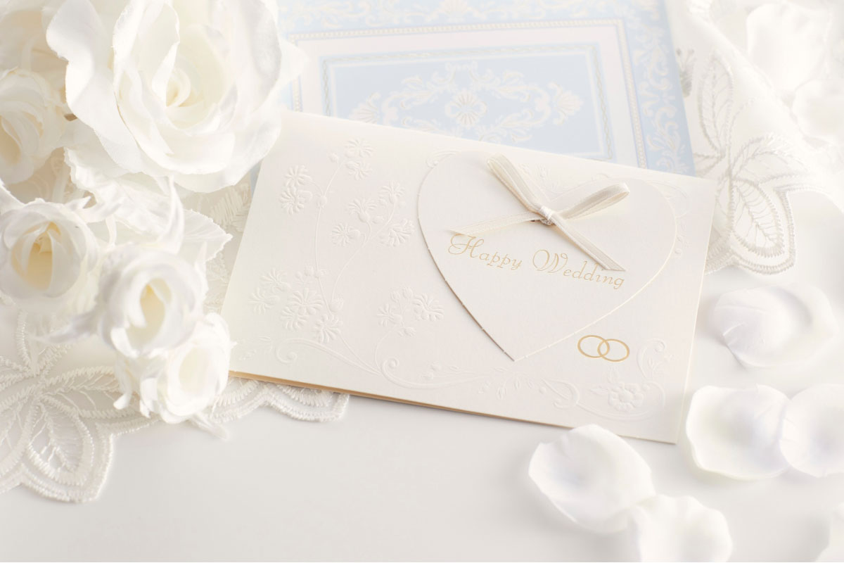 Cream Happy Wedding card with heart detail, white flowers and scattered petals.