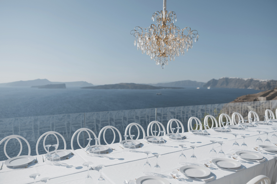 White table and chairs set for dinner overlooking blue water with chandelier 