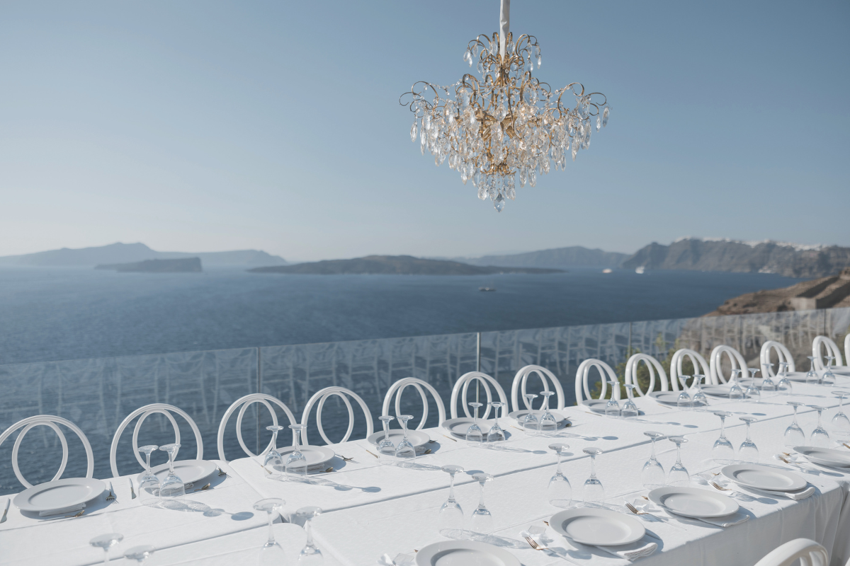 White table and chairs set for dinner overlooking blue water with chandelier