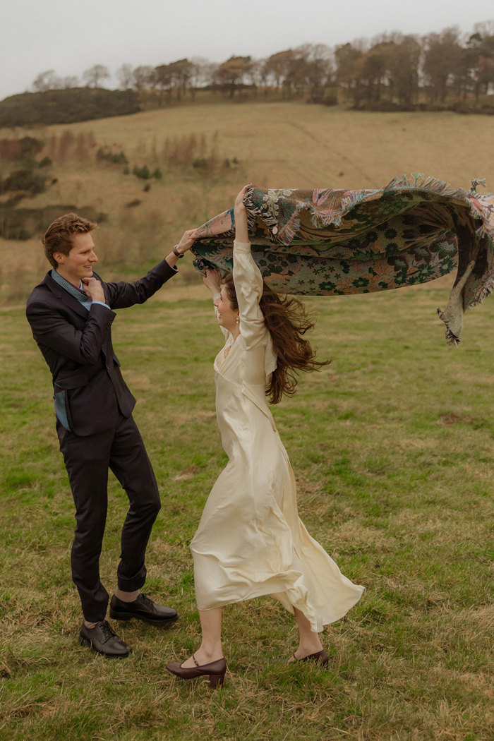 bride holds up paisley print scarf as the wind blows it into the air 