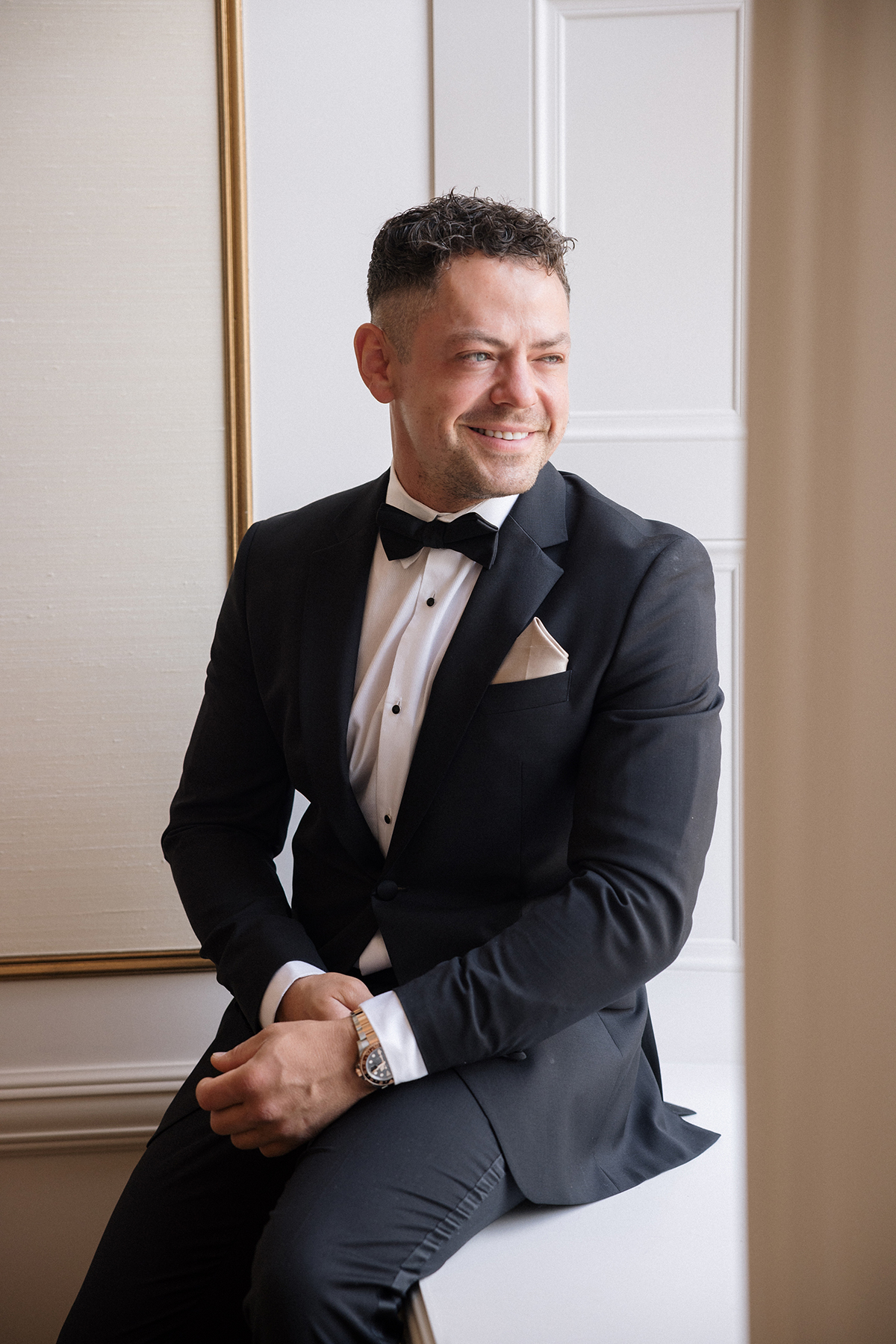 Groom in a black tuxedo sitting by a window before the wedding ceremony