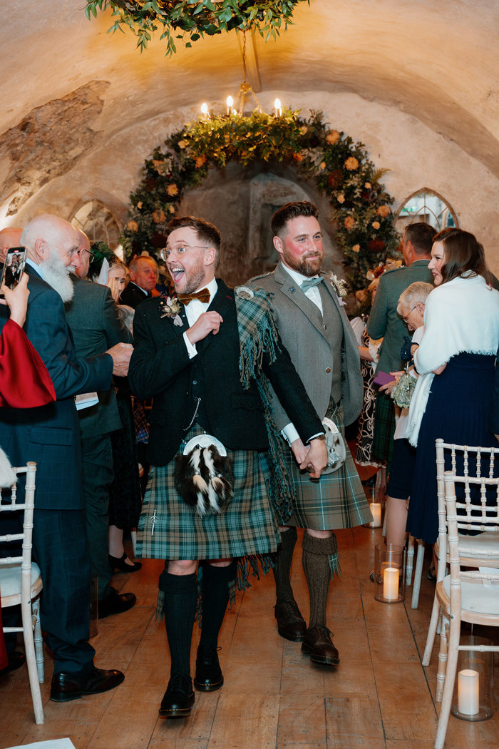 two grooms holding hands walking back up the aisle together after their neidpath castle wedding ceremony
