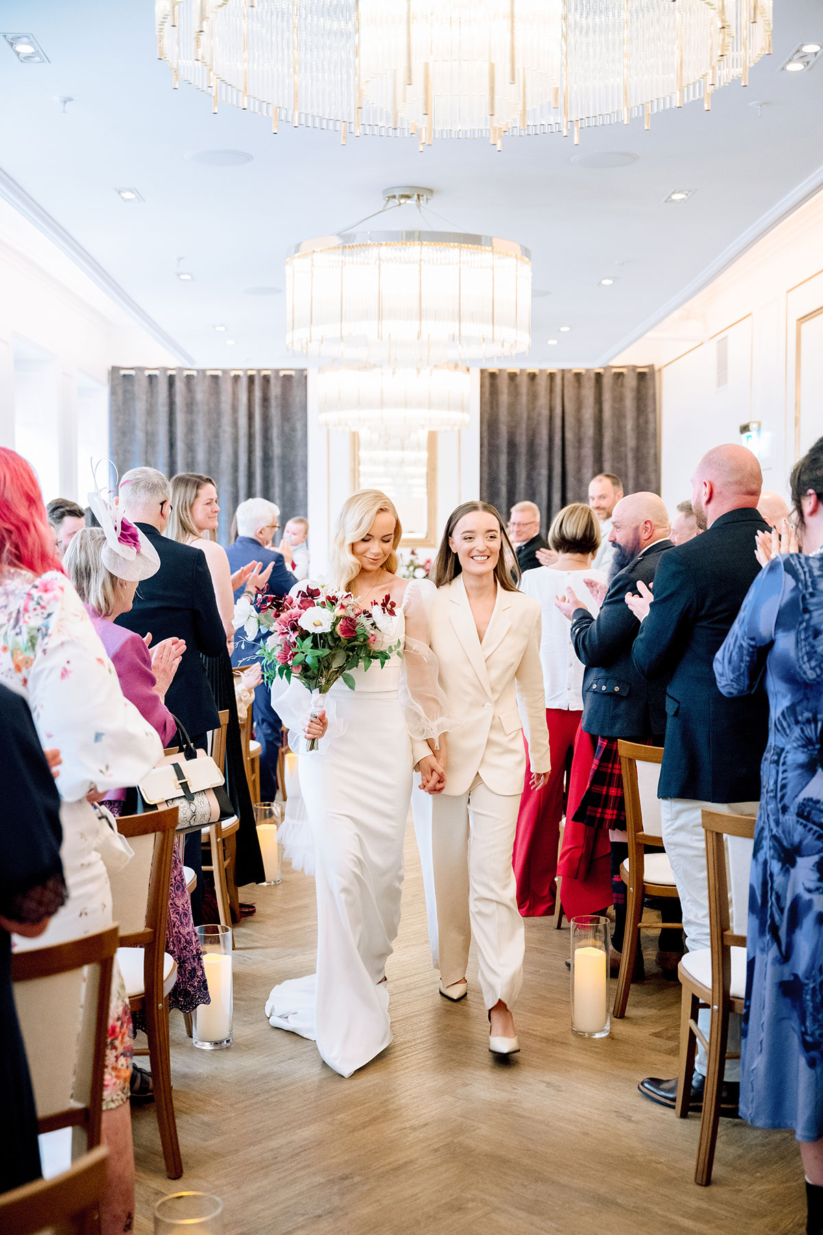 two brides walk up the aisle at the exchange holding hands