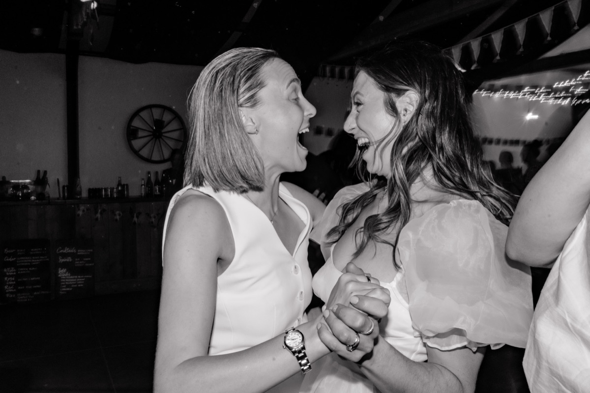 Black-and-white photo of Hannah and Donna laughing and dancing together at their Harvest Moon wedding reception.