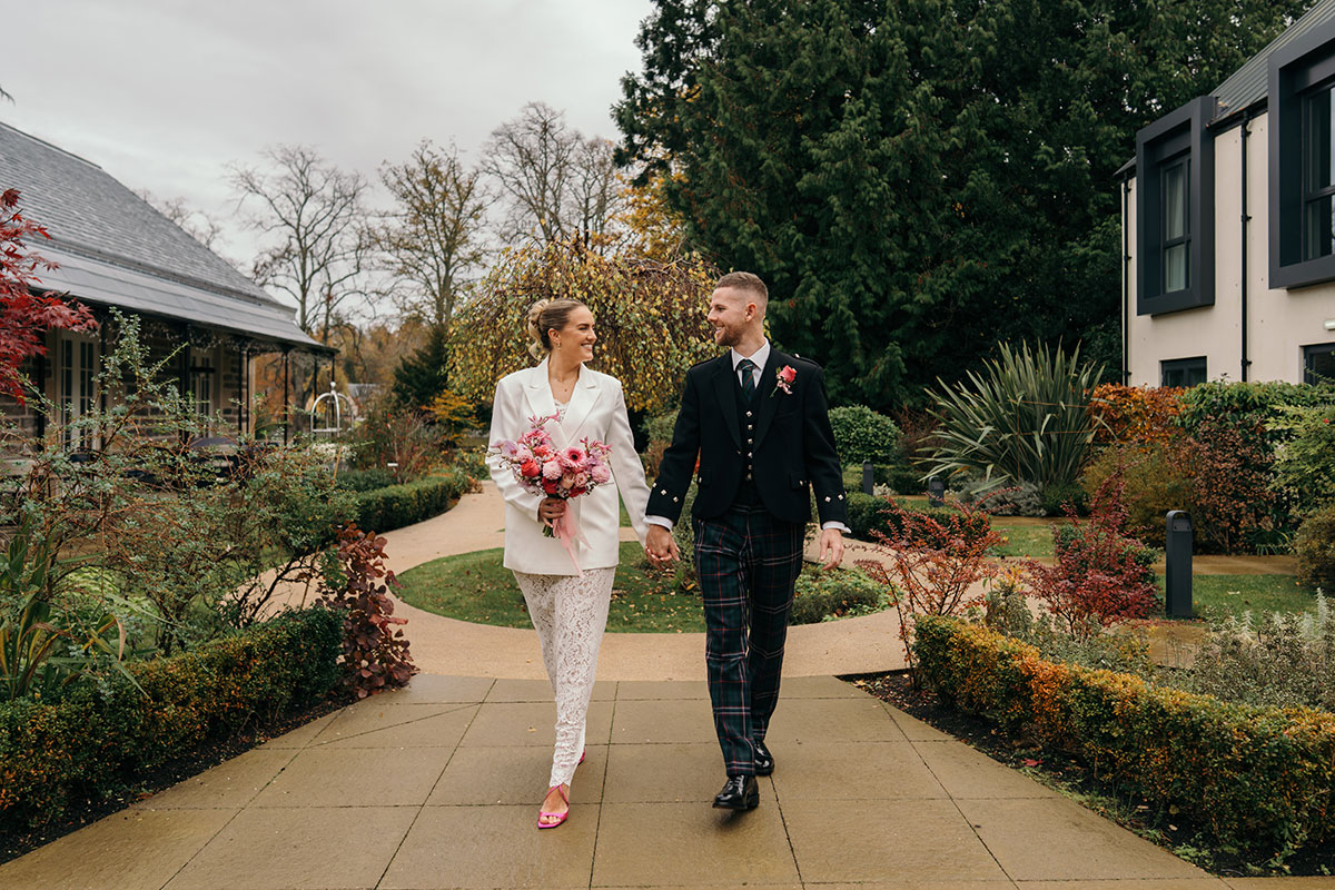 Bride and groom holding hands walking through landscaped wedding venue grounds in Scotland