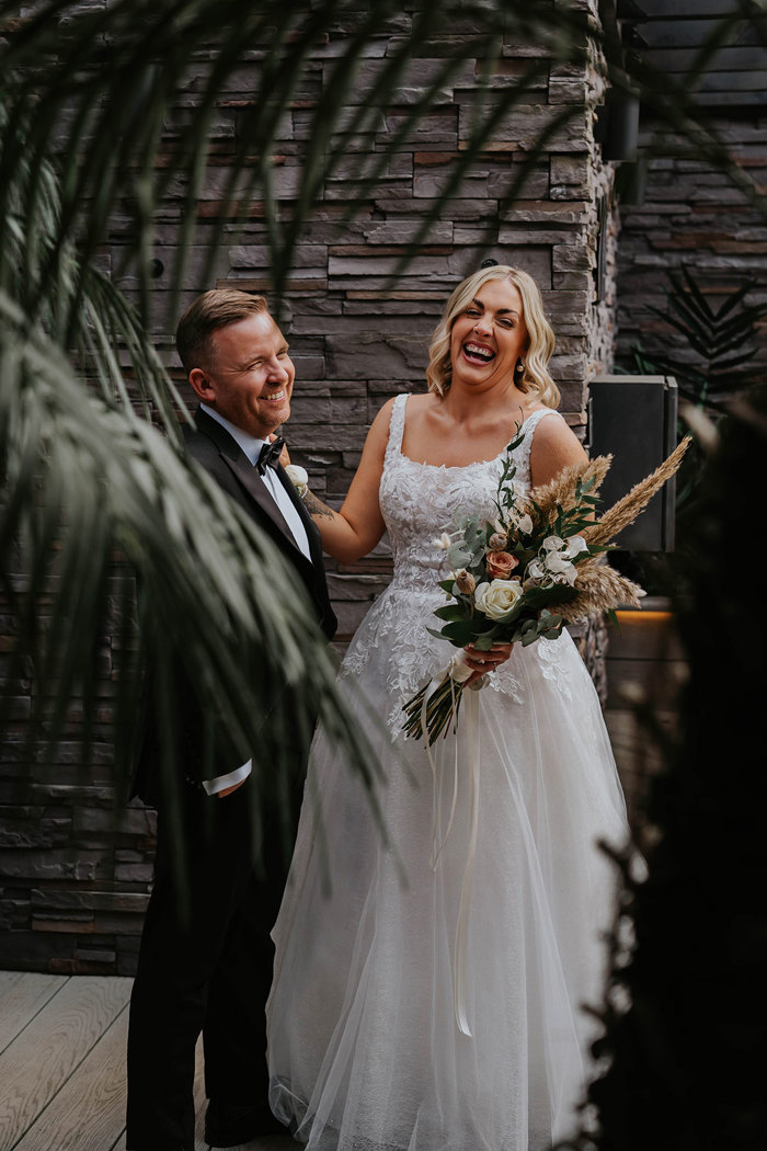 A bride and groom laughing while posing for a picture.