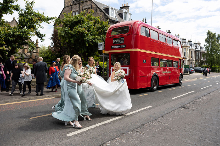Bride walks across road with bridesmaids holding her dress up