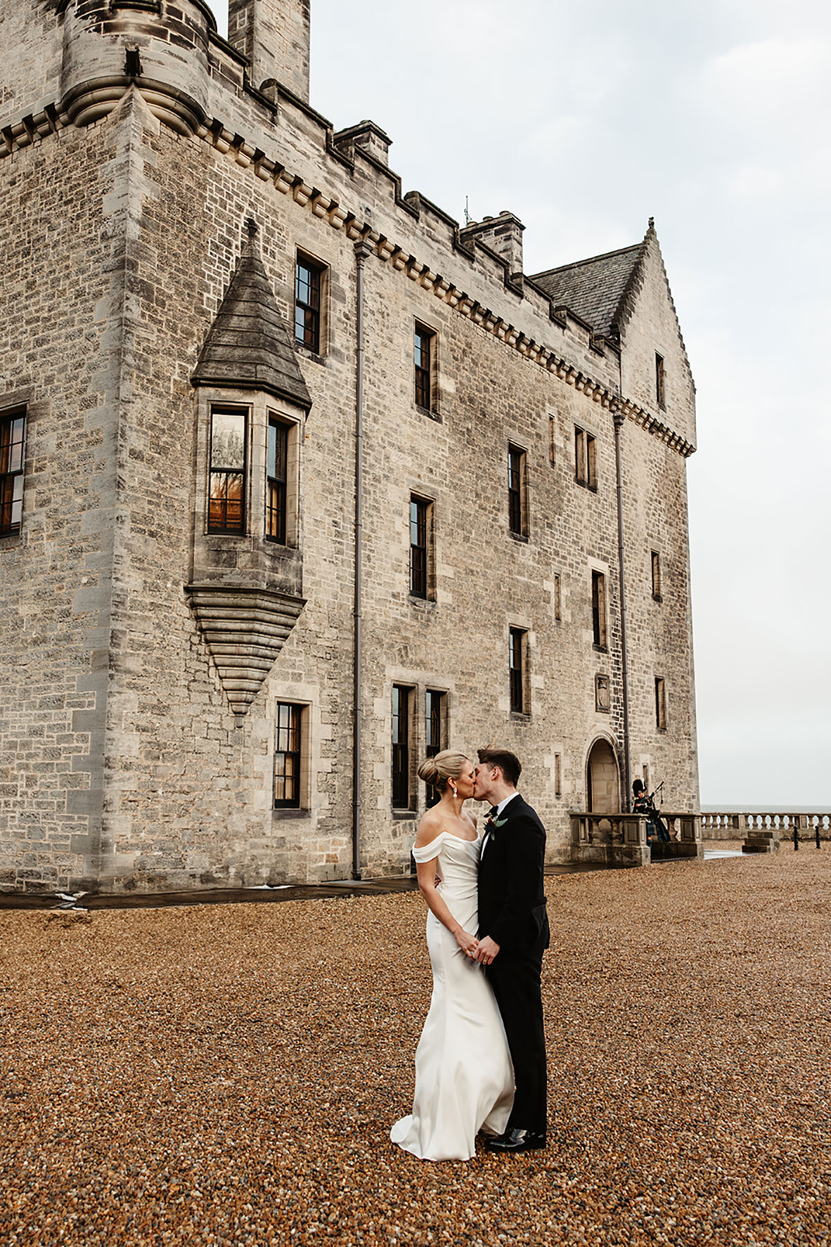 Bride and groom sharing a kiss outside the stone exterior of Barnbougle Castle.