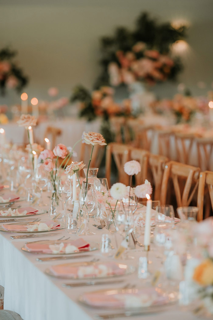 Table decor with pink napkins and pink flowers in small vases along the length of the table