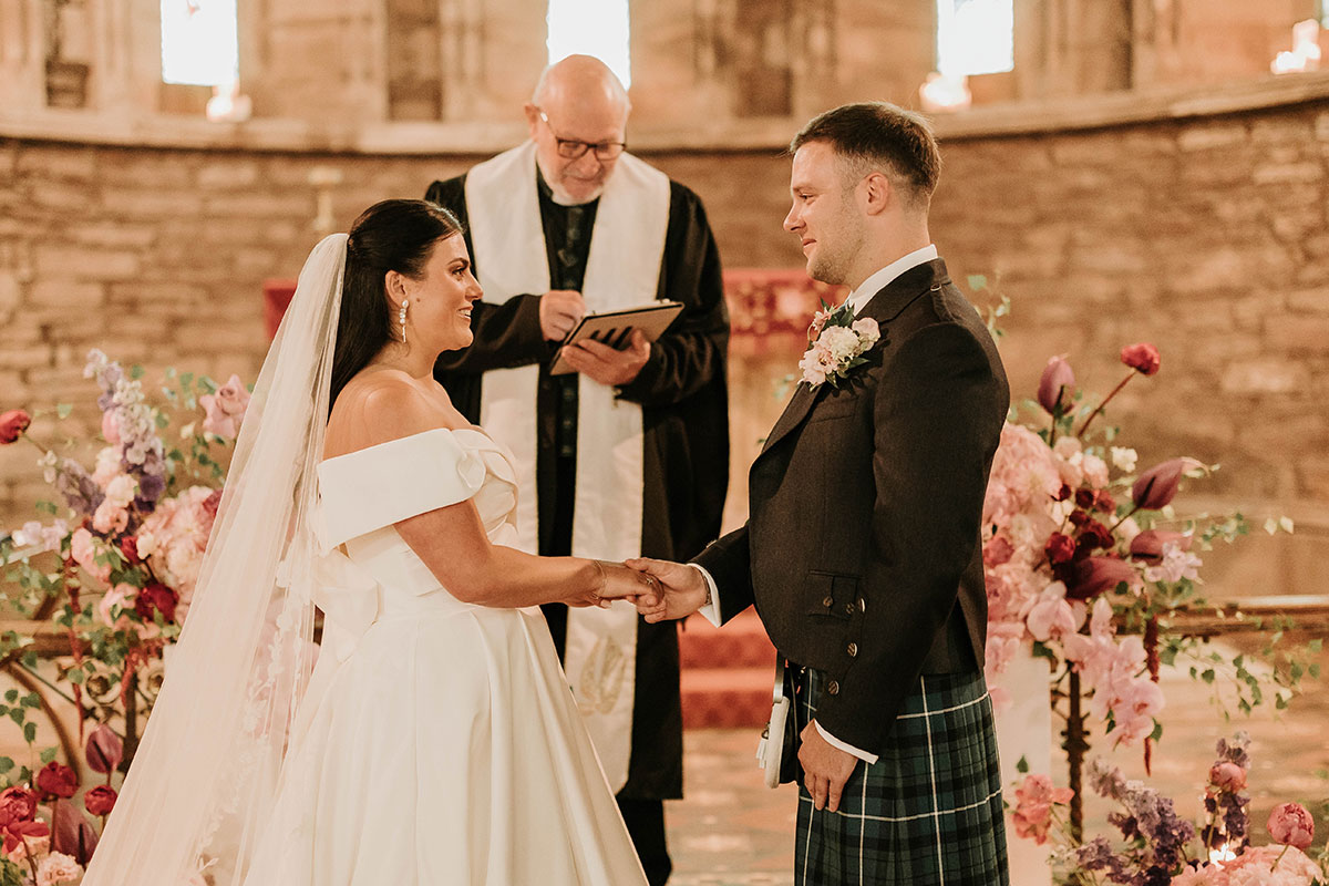 Bride and groom holding hands during ceremony with minister in St Palladius Church Drumtochty Castle Aberdeenshire