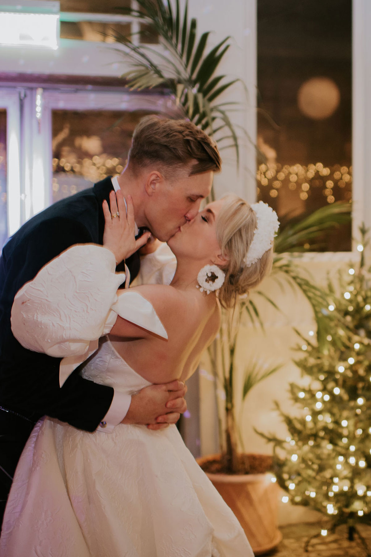 A bride and groom kiss in front of fairylights