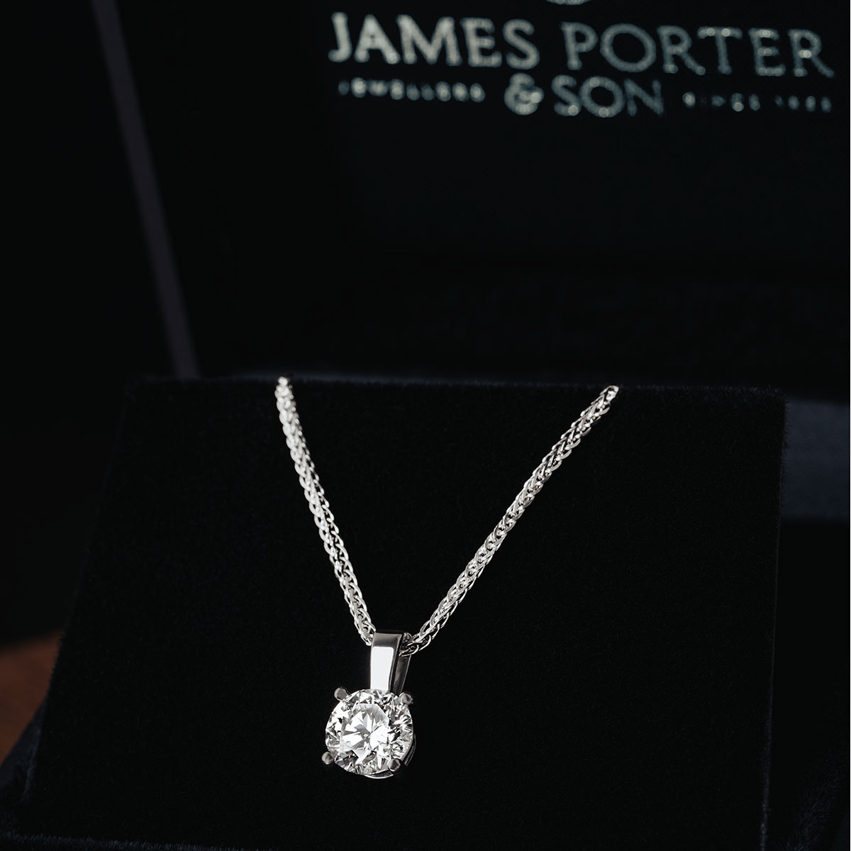 a lab-grown diamond solitaire pendant on a white gold chain in a black box