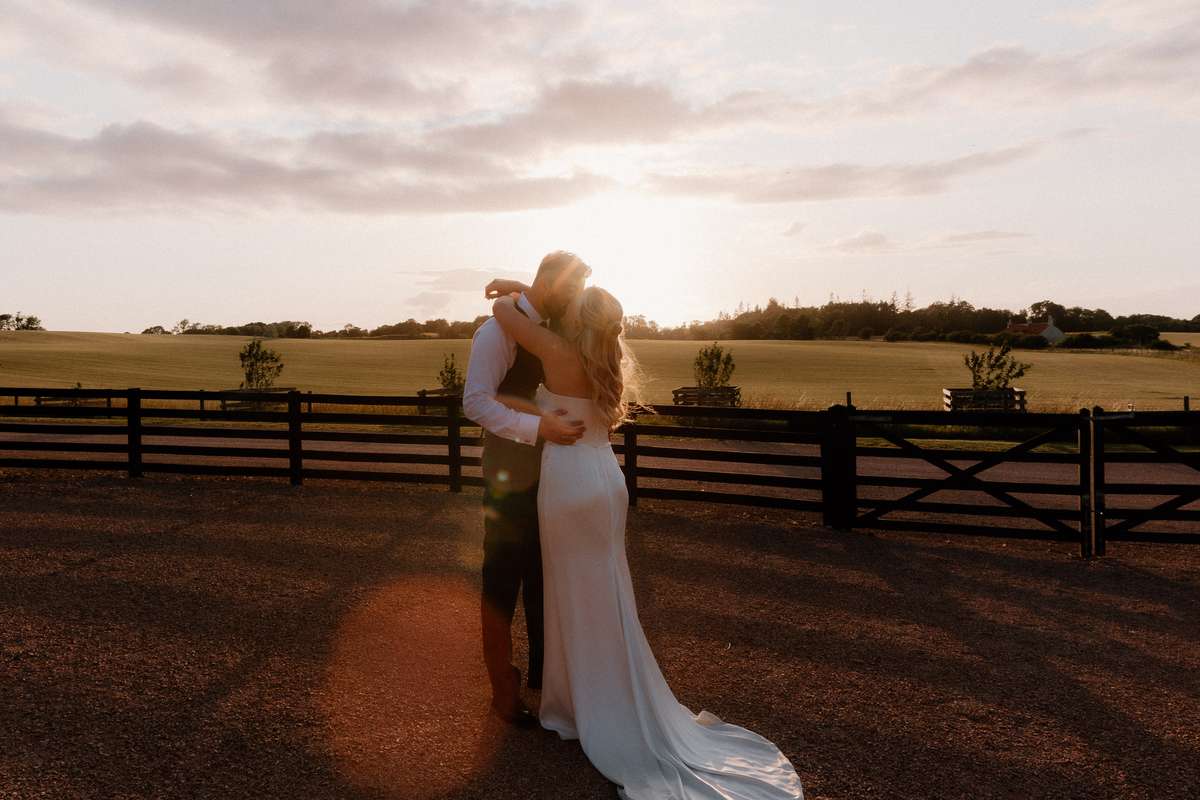 Bride and groom embracing at sunset outside Falside Mill wedding venue overlooking the Fife countryside