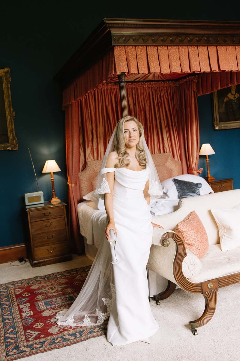 Bride Lia poses in her Renhue wedding dress and lace-edged veil while getting ready at Cambo House.