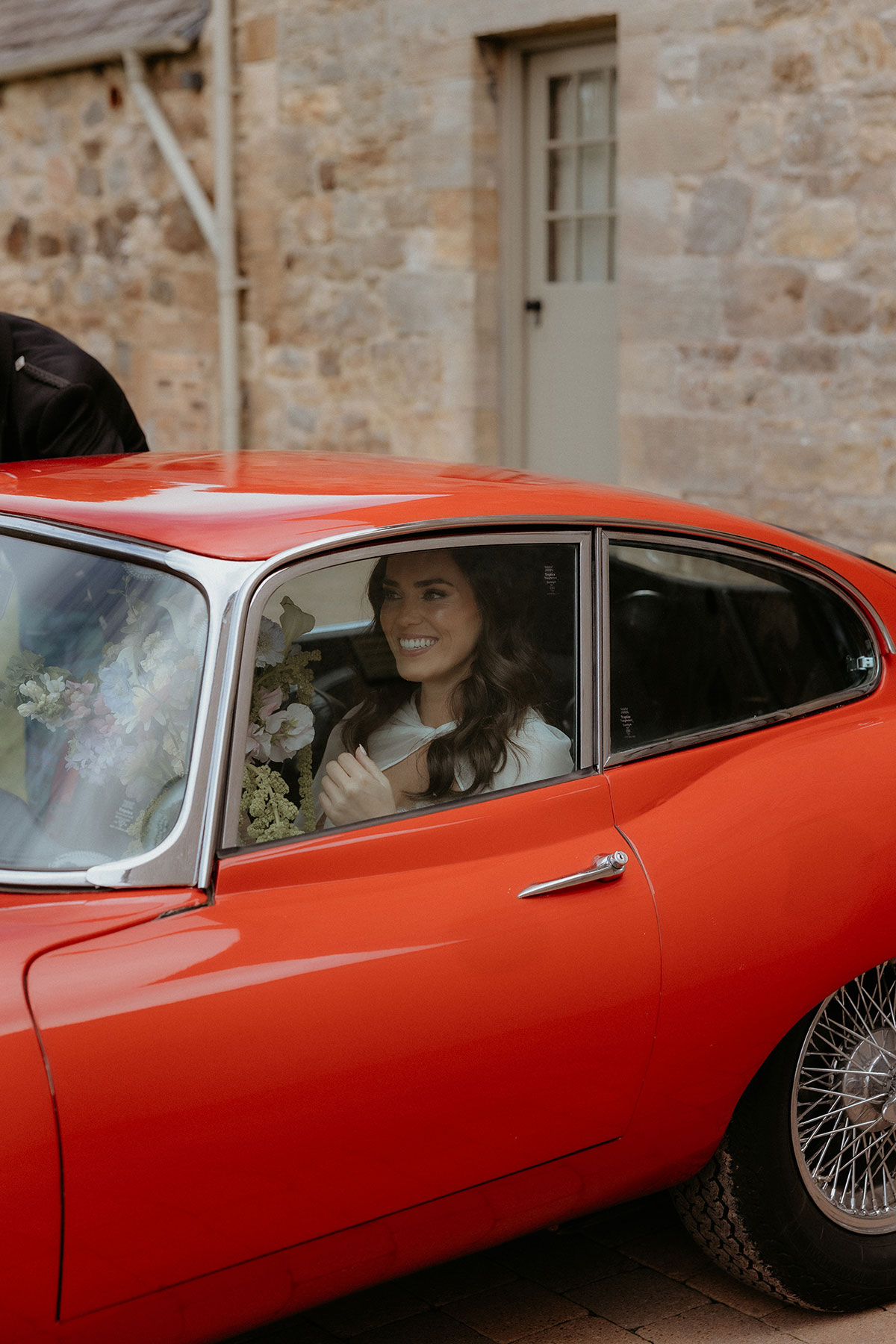 Bride smiling inside classic red E-Type Jaguar outside Rosebery House and Steading, Midlothian wedding venue.