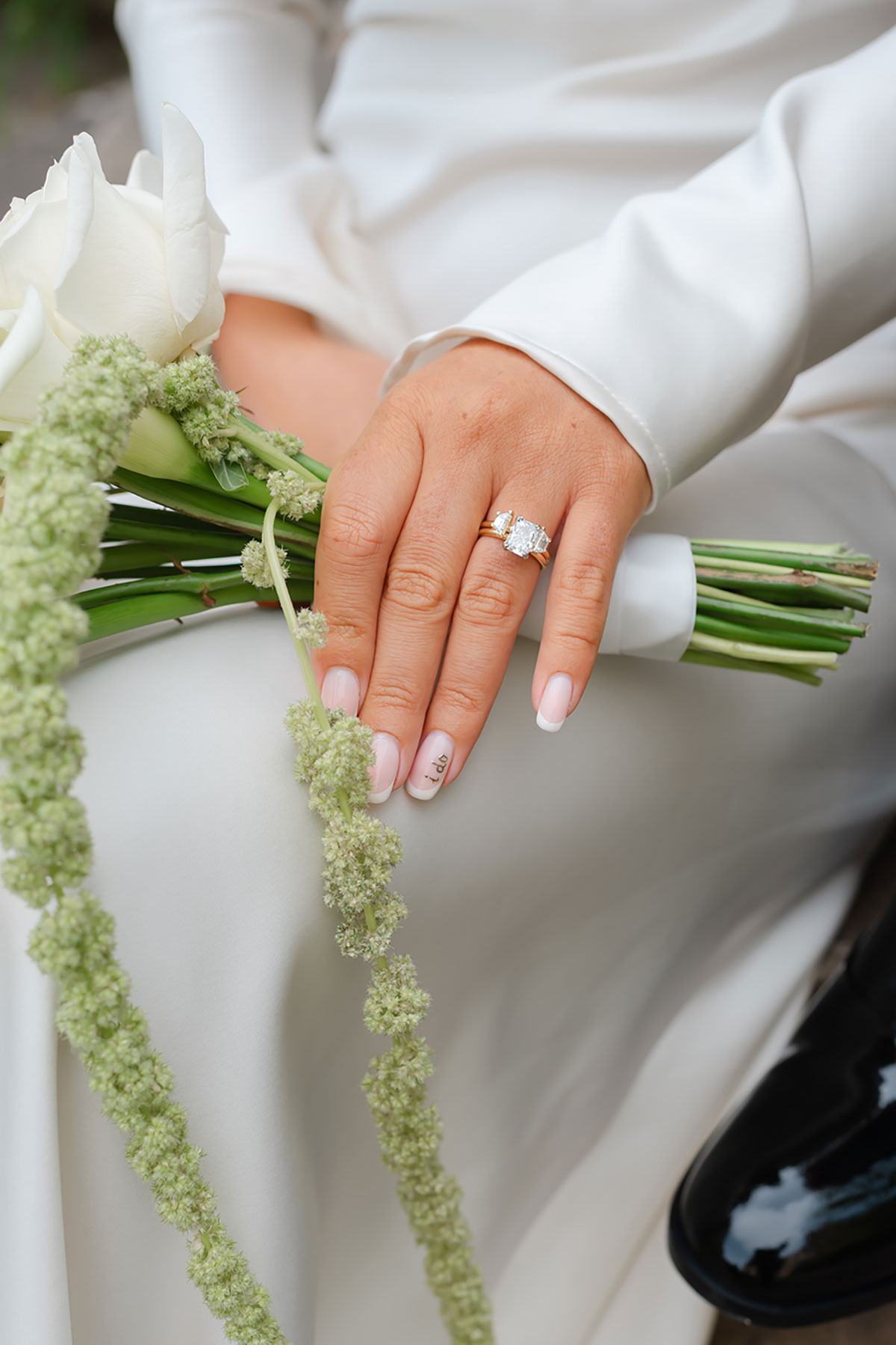 Close-up of bride’s hand showing engagement ring and wedding manicure with ‘I do’ detail, holding white rose bouquet
