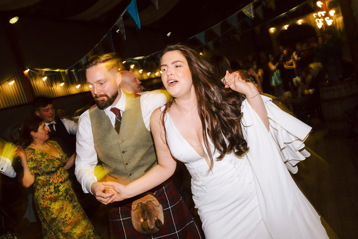 A man and woman ceilidh dancing with their arms around each other with other couples dancing in the background
