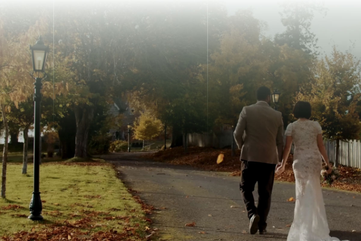 bride and groom walking on a park path holding hands on an autumnal day