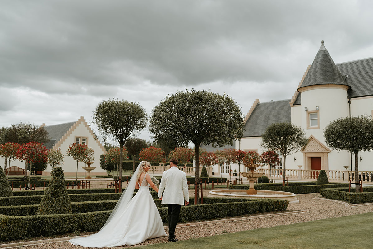 Bride and groom walking through formal gardens at Ingliston Country Club grounds