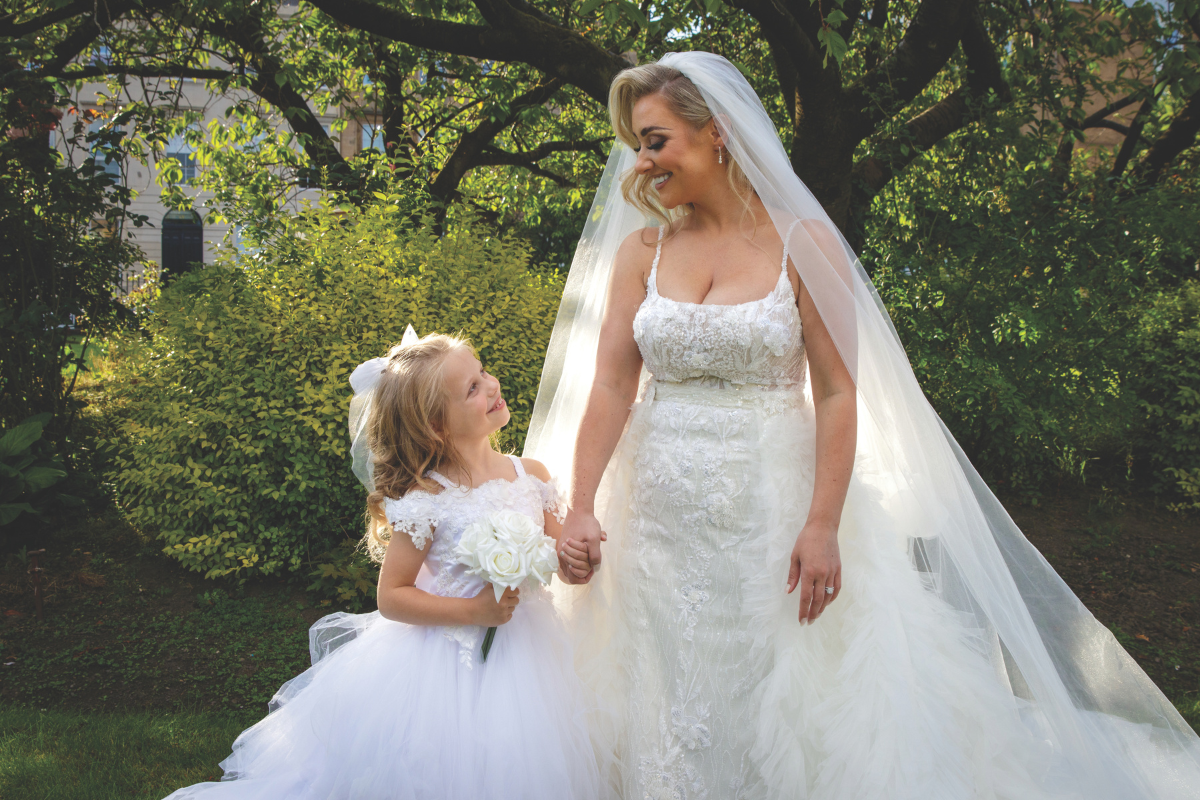 Bride and flower girl in white dresses looking at each other whilst holding hands