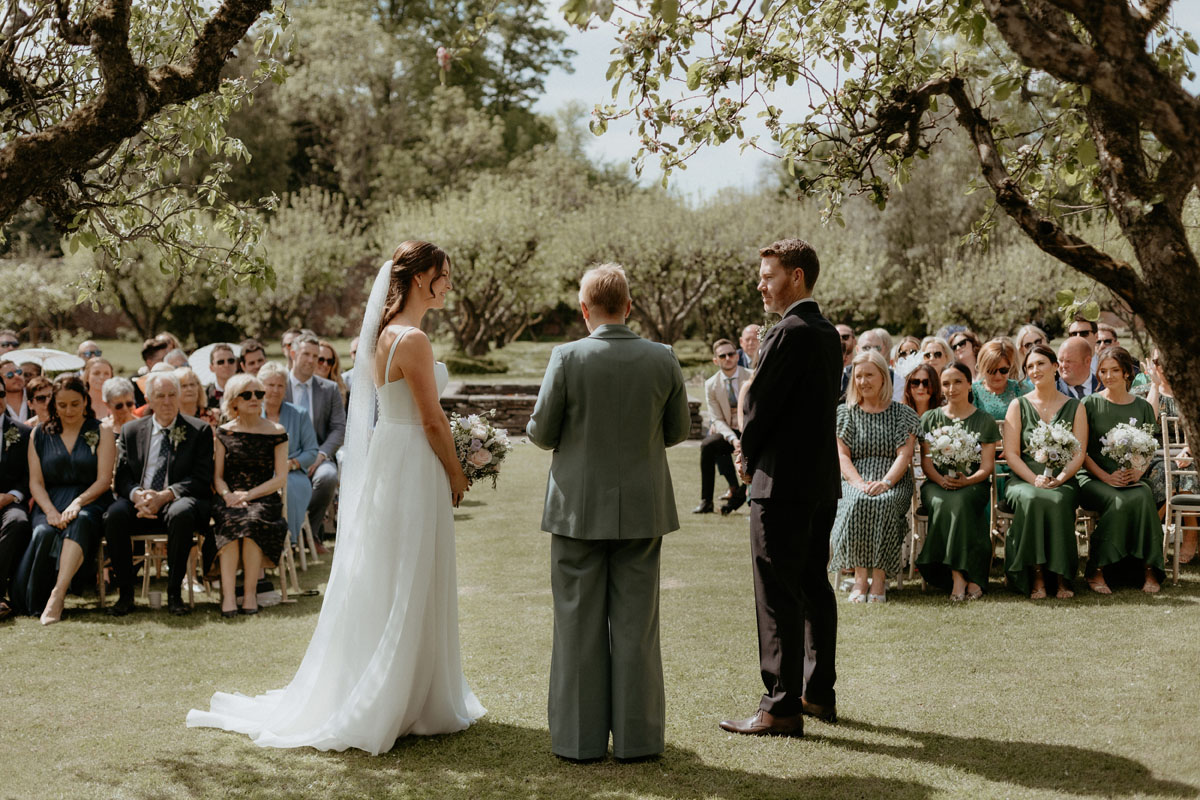 Bride and groom standing with their celebrant during an outdoor wedding ceremony at The Byre at Inchyra.