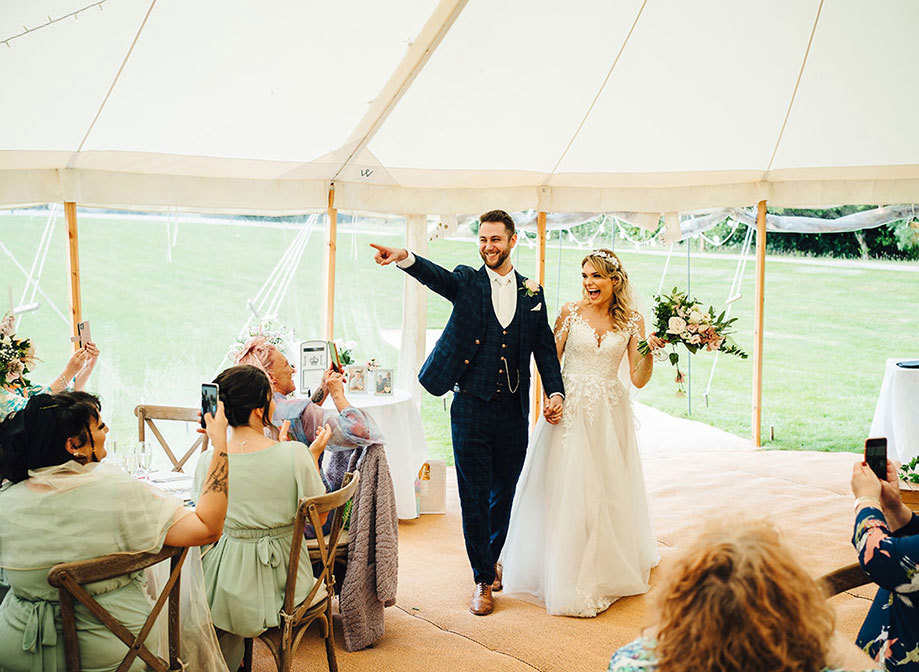Newly-wed couple are welcomed into their marquee reception by friends and family