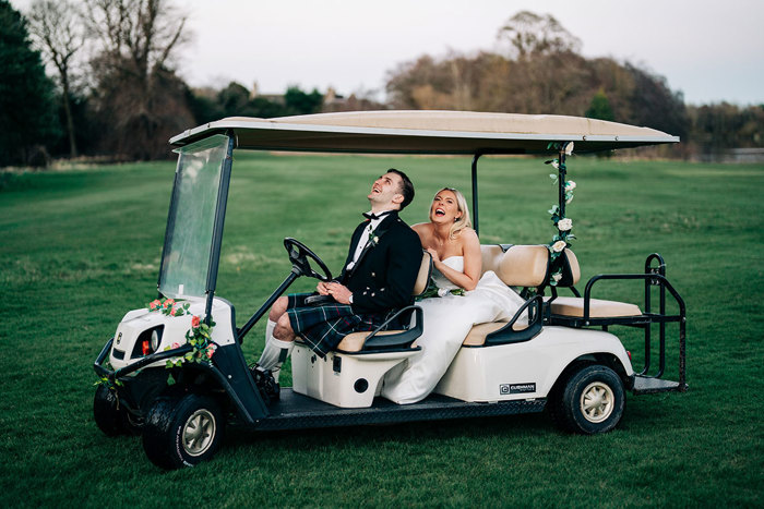 a laughing bride and groom on a golf buggy on a lawn