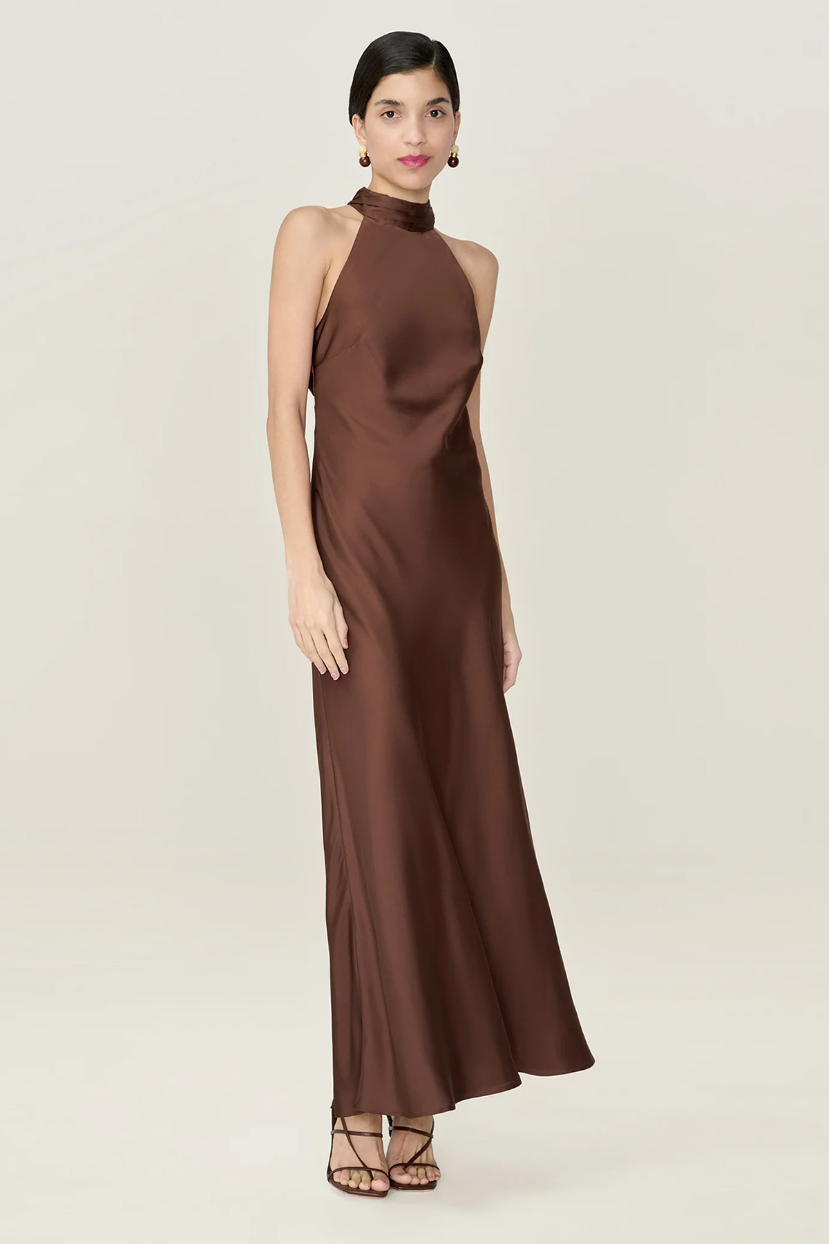 Model wearing a chocolate-brown satin halterneck maxi dress with a high neckline and flowing silhouette.