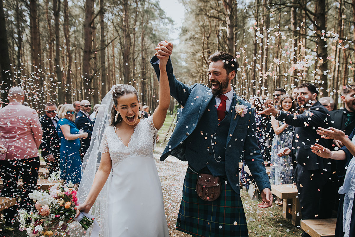 bride and groom cheer as wedding guests throw confetti over them at harvest moon