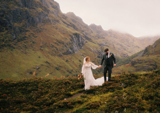 bride and groom hold hands as they walk through the scottish hills on wedding day