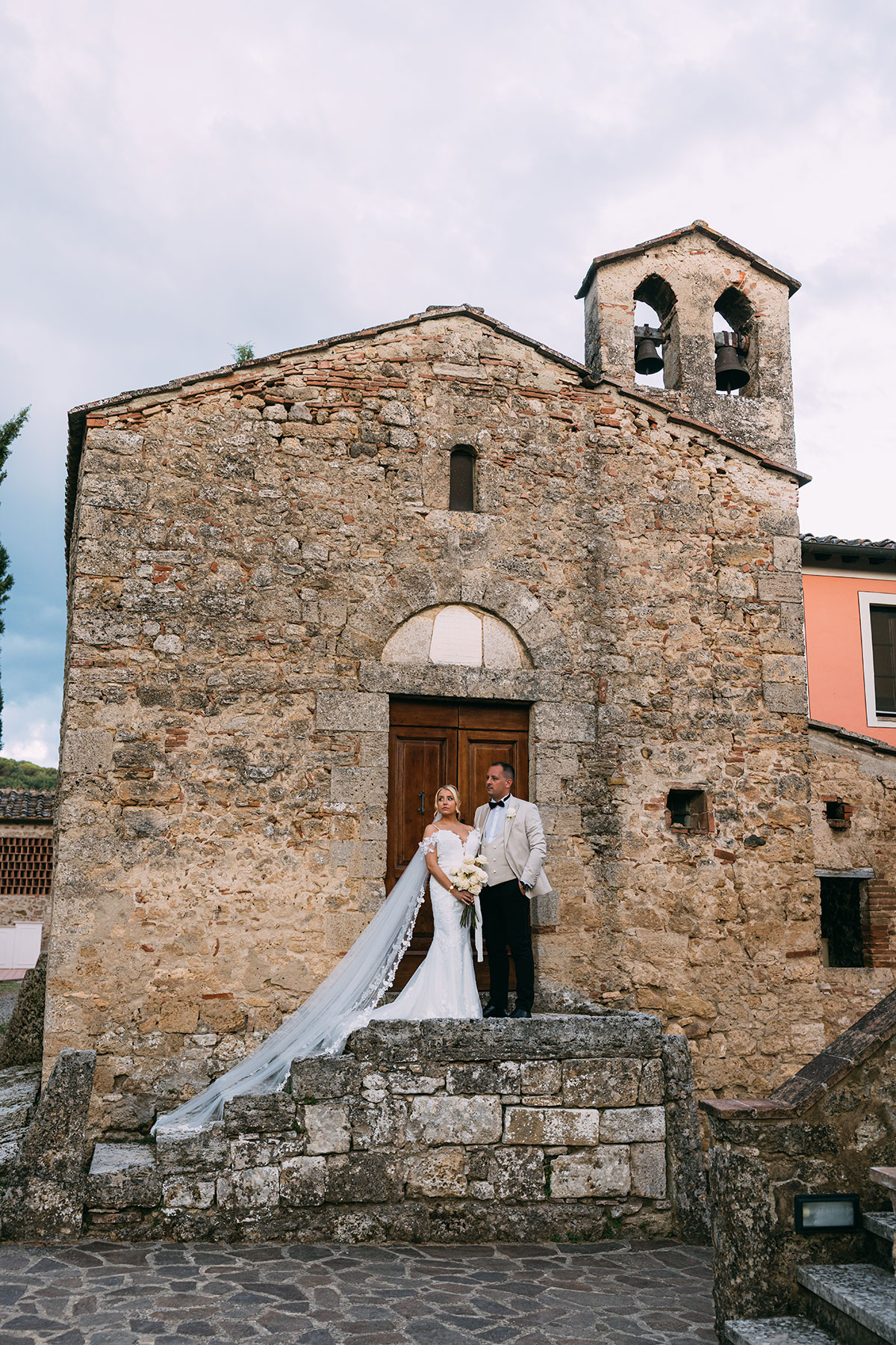 Bride and groom outside rustic stone church at Antico Borgo San Lorenzo Tuscany wedding venue
