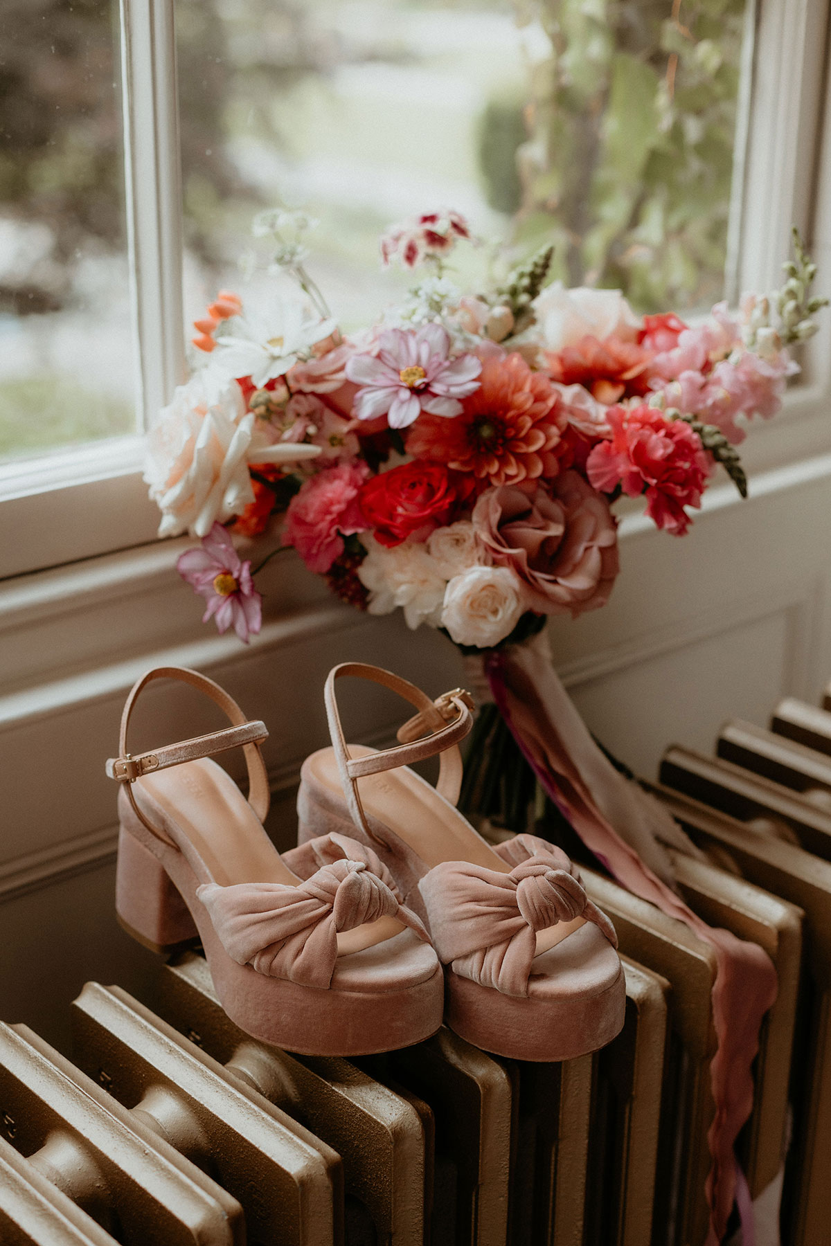 a colourful bouquet and peach velvet shoes sitting on a radiator by a window