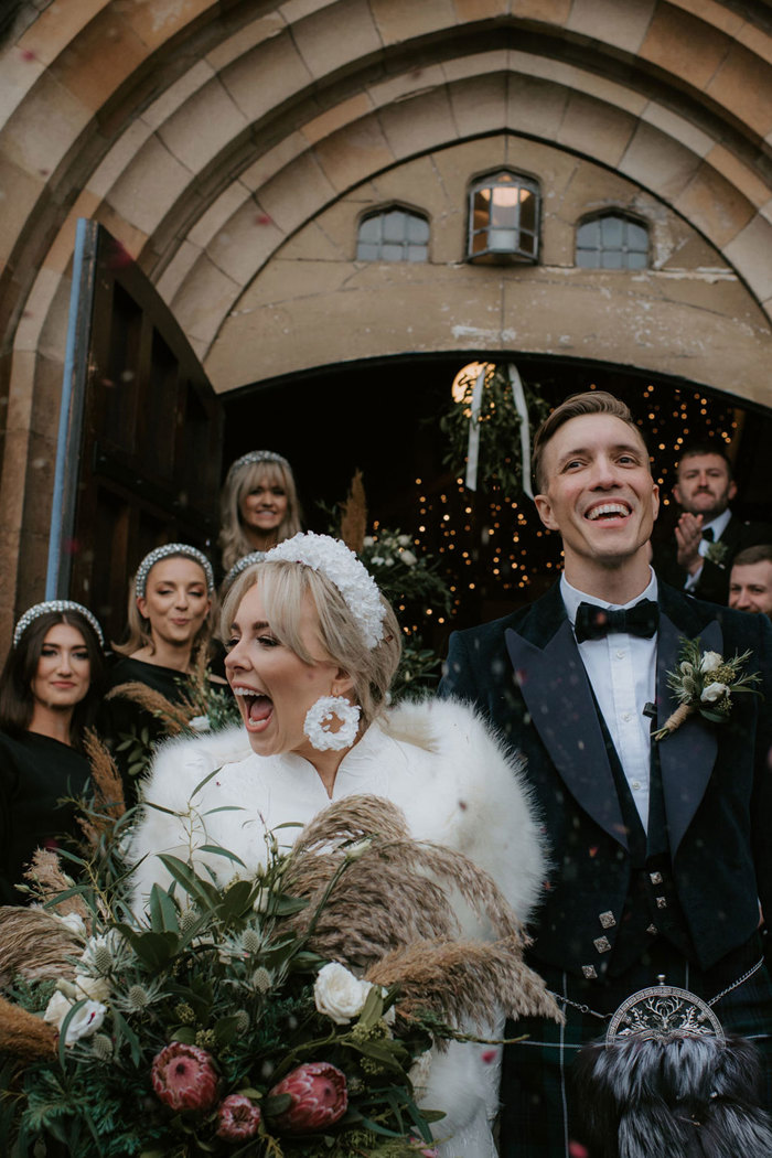 A bride and groom leave the church with their wedding party behind them 