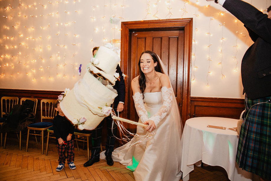 A Person Wearing A Wedding Dress With Lace Sleeves Hitting A Pinata Wedding Cake With A Stick