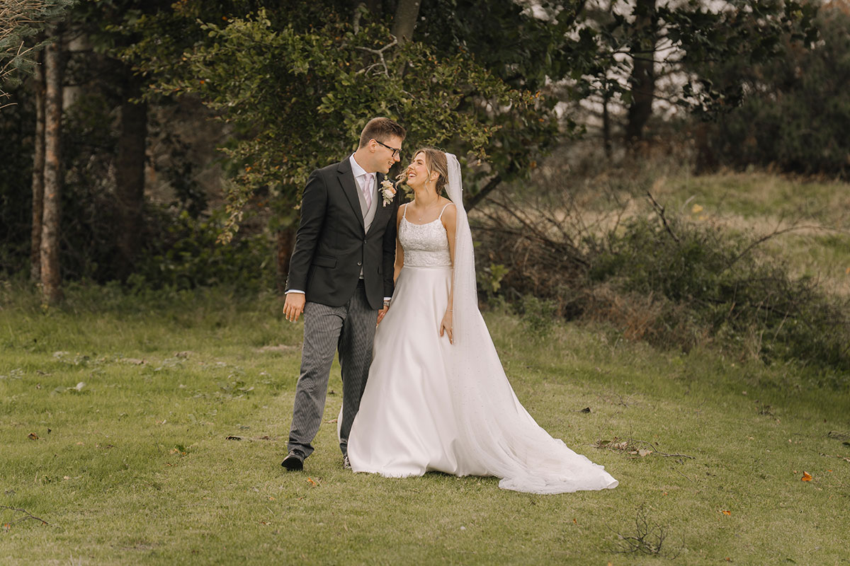 Bride and groom walking hand in hand across the lawn during relaxed outdoor wedding photos