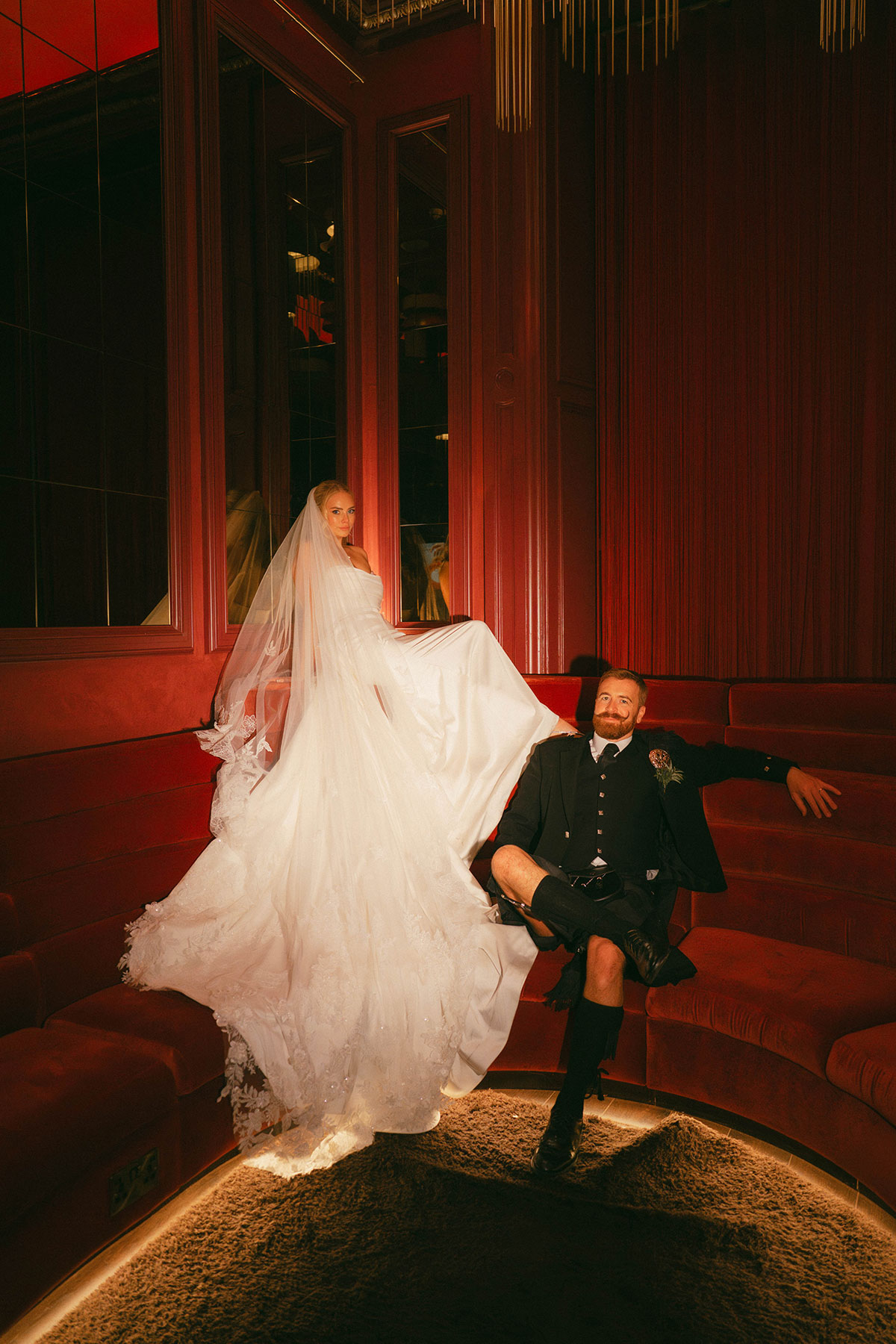 bride and groom posing in red velvet lounge with dramatic lighting and mirror panels