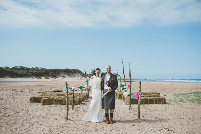 bride and groom stand under wooden arch way on harvest moon beach