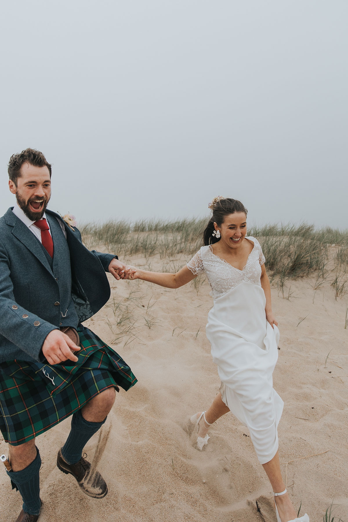 bride and groom hold hands as they run down a sand hill at harvest moon weddings