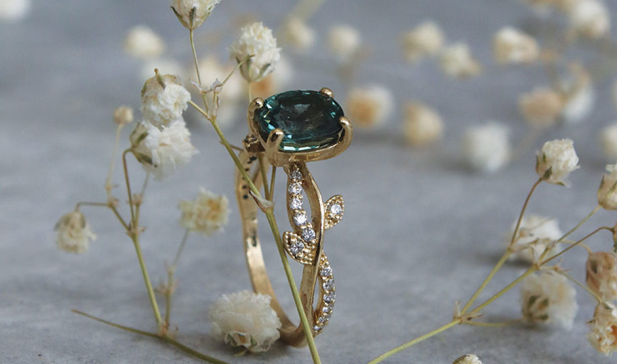 a gold ring with a blue stone and diamonds on it by Christina Rose Leon Jewellery surrounded by small white gypsophila flowers