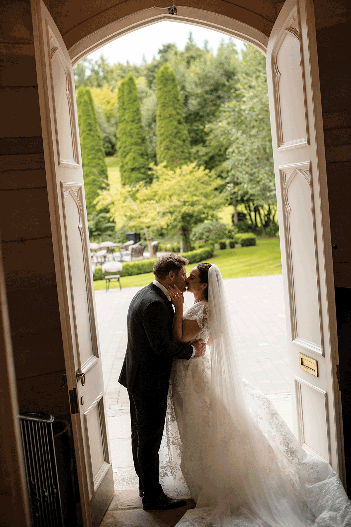 Newlywed couple kissing in the doorway of a country house wedding venue, framed by open doors and garden views beyond