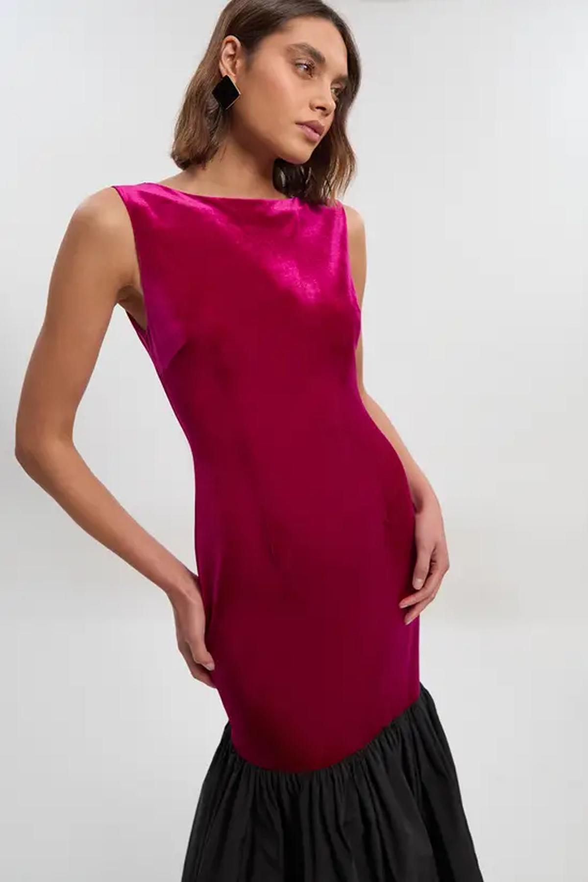 Model wearing a hot-pink velvet midi dress with a boat neckline and contrasting black gathered hem.