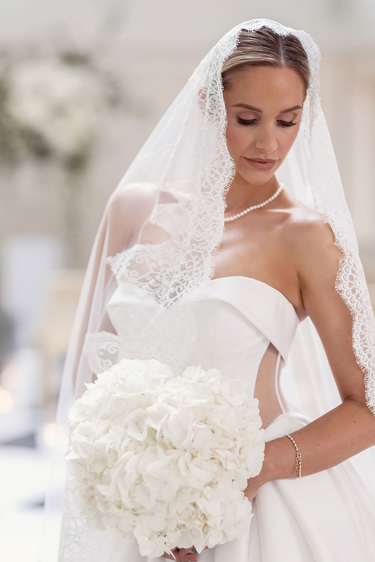 Model Emily Shak in strapless wedding dress with lace veil holding white hydrangea bridal bouquet