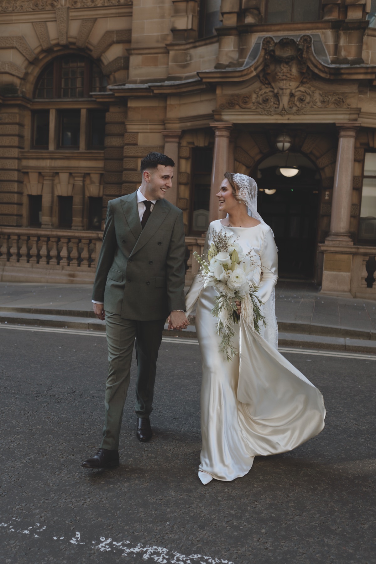Newlyweds walking hand in hand through Glasgow city centre after their wedding ceremony.