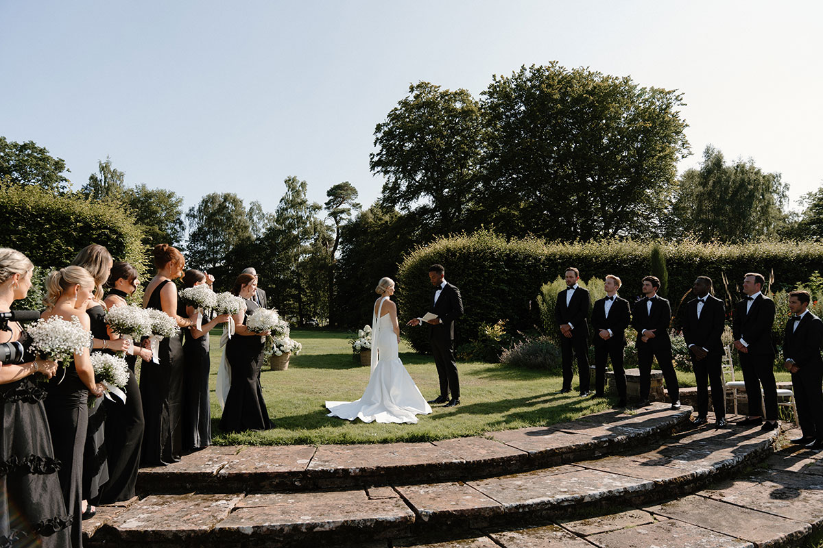 Outdoor wedding ceremony in a Scottish garden venue with bridesmaids, groomsmen and guests gathered in the sunshine